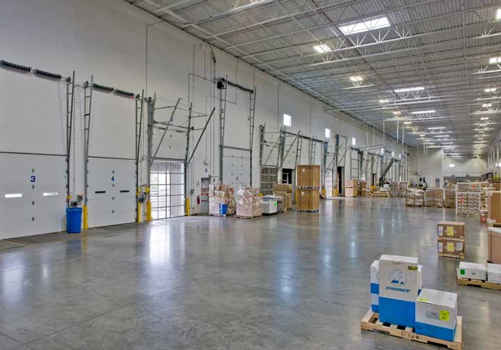A long shipping and delivery warehouse with open bay doors lines the tall left-hand walls, while the ample space is filled with pallets of equipment and goods for Nippon Express, the second project done by Keeley Construction, Inc.